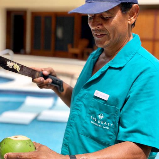 The Coast Beachfront Hotel employee, Antonio, cutting open a coconut for a guest